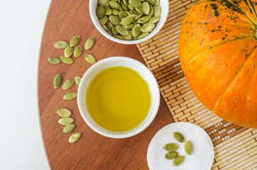 Small bowl with pumpkin seed oil and cotton pad. Ingredients for preparing homemade face or hair mask. Natural beauty treatment recipe, zero waste concept. Top view, copy space