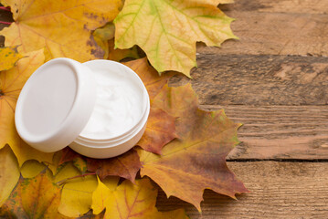 jar of face cream on yellow autumn leaves on wooden background