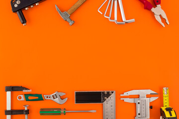 Work tool of the wizard. Tape measure, screwdriver, hammer, wrenches, clamp, screws, drills and other tools on a orange surface.