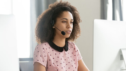 African American female call center operator in wireless headset using computer, looking at screen,...