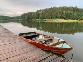Obraz premium Wooden boat on the pier on the background of the lake. Fishing boat on the shore of a forest reservoir. The boat is tied to the shore. Concept: outdoor recreation, tranquility by the water.