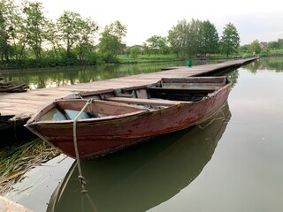 Wooden boat on the pier on the background of the lake. Fishing boat on the shore of a forest reservoir. The boat is tied to the shore. Concept: outdoor recreation, tranquility by the water.