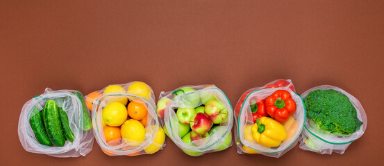 Wide banner Fresh ripe and juicy fruits and vegetables in reusable eco friendly mesh bags on the brown background. Plastic free, zero waste, and sustainable living concept. Reusable using. Copy space.