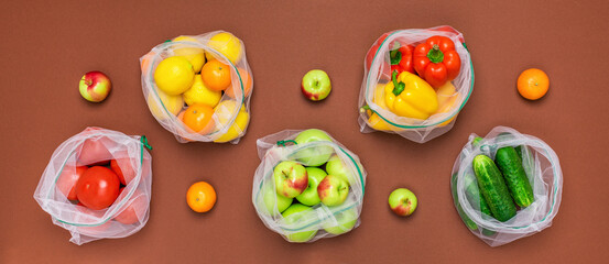 Wide banner Fresh ripe and juicy fruits and vegetables in reusable eco friendly mesh bags on the brown background. Plastic free, zero waste, and sustainable living concept. Reusable using. Top view.