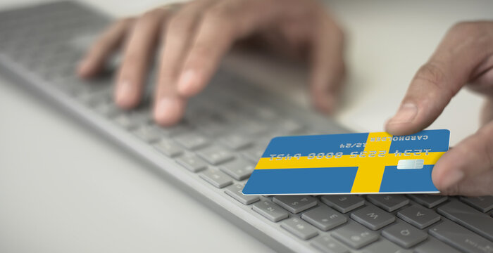 Man pays online with plastic bank card with printed flag of Sweden. Fictional numbers