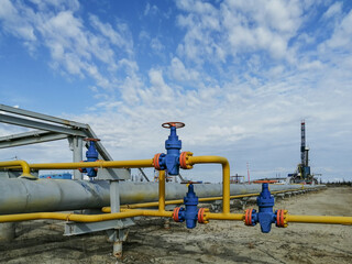 Pipeline fittings and manifold of producing gas wells in the field. Handwheels for high pressure valves. In the background, a drilling rig. Blurring distant objects.