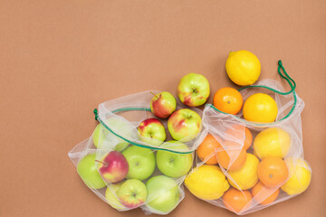 Ripe and juicy fruits lemons apples and tangerines in reusable eco friendly mesh bags on the brown background. Plastic free, zero waste and sustainable living concept. Reusable using. Copy space.