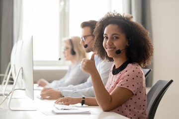 Smiling mixed race female call center operator, agent in wireless headset showing thumbs up...