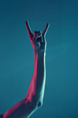 Male hand in the goat gesture isolated on neon blue light background. Concept photography, music poster, rock and roll
