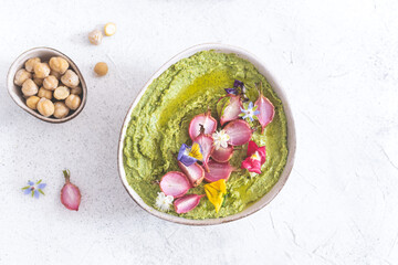 Colorful green hummus bowl with baked radish and edible flowers, vegetarian meal, top view