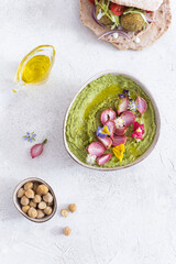 Fototapeta na wymiar Colorful green hummus bowl with baked radish and edible flowers, vegetarian meal, top view