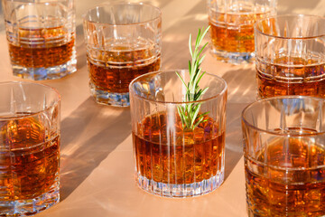 Many glasses of cold whiskey with rosemary on beige.