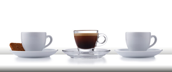 A row of 3 glass and white expresso cups and saucers full of smooth expresso coffee, on a white style bar or table top on white