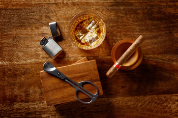 View of a crystal glass of golden whisky, cigar and cigar cutter and petrol lighter, shot from above on a dark wood