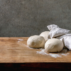 Dough for pizza cooking. Three balls of fresh homemade wheat dough under linen cloth on wooden kitchen table. Home baking.