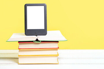 Reading. E-book stands on a stack of books on a yellow background. Copy space. Mock up. Concept of education and electronic gadgets