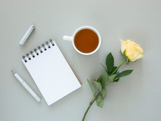 Festive desktop mockup. Rose flower, cup of tea and blank paper spiral notebook with space for greetings. holiday concept