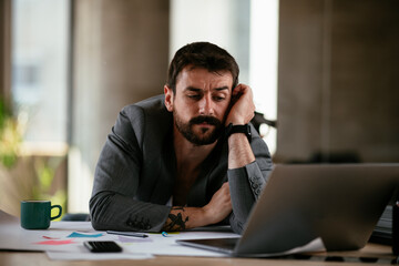 Naklejka premium Tired businessman working with laptop at office. Businessman sitting at office desk working on laptop computer..