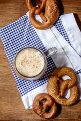 Glass of lager beer with traditional salted pretzels on white and blue napkin over wooden background. Flat lay, space. Oktoberfest theme