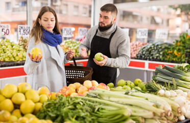 Smiling male seller assisting customer to buy apples in grocery shop. High quality photo