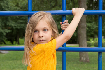 Fototapeta premium A beautiful six-seven-year-old girl with blond hair in a bright yellow jumpsuit climbing stairs in the playground
