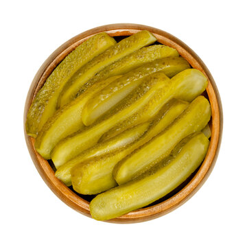 Sliced pickled cucumbers, also known as pickle or gherkin, in a wooden bowl. Small pickled cucumbers with bumpy skin, sliced lengthways. Baby pickles. Close-up from above over white, macro food photo.