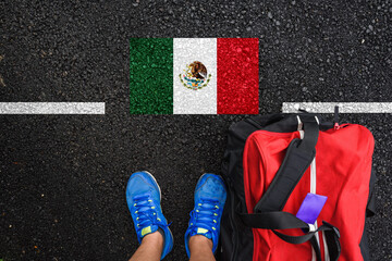 a man with a shoes and travel bag is standing on asphalt next to flag of Mexico  and border 
