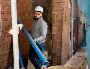 Focused bearded guy working with metal-reinforced plastic pipes at indoors building site