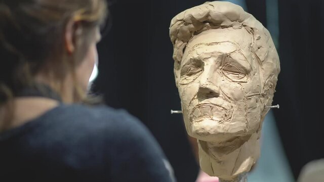Woman sculptor at work on a sculpture of a human head. The process of restoring the shape of the portrait. Side view. Close up view.