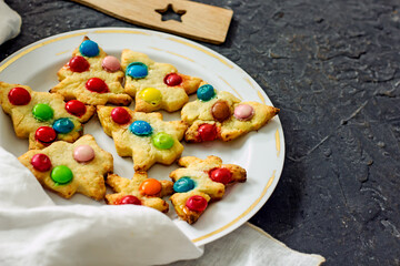 Colorful christmas homemade christmas tree cookies on white plate on dark background, copy space
