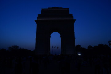Fototapeta na wymiar Silhouette of India Gate, a war memorial, with three army flags and surrounding greenery at sunset, Delhi, India