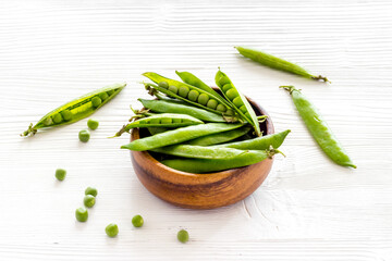 Green pea pods in wooden bowl on the kitchen background