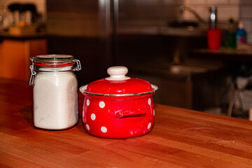 Red saucepan with speckled print with sugar jar on table in the kitchen