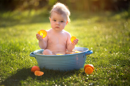 Little toddler boy bathes in the park with oranges and soap bubbles.