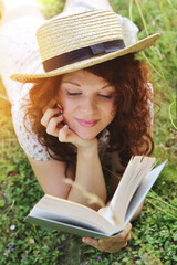 jeune et jolie femme rousse allongée dans l'herbe et lisant un livre 