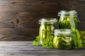 Healthy fermented food. Three glass jars of homemade fermented cucumbers with garlic, dill and pepper. Rustic background. Copy space.