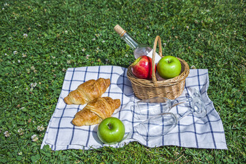 Romantic summer picnic lunch outdoors. Wicker basket with croissants, apples and bottle of rose...