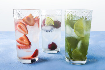 Three glass of refreshing cool detox drink with strawberry, lime, cherry and mint on blue background. Various summer lemonades or ice tea. Mojito cocktails with ice cubes. Healthy eating. 