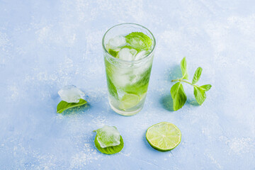 Refreshing cool detox drink with lime and mint on blue background. Summer lemonade or ice tea in a glass. Mojito cocktail with ice cubes. Healthy eating. Сopy space for text