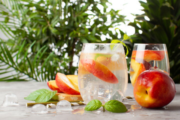 Peach cocktail or lemonade with fresh peaches and tropical plants on background.Close up of refreshing summer cocktail.