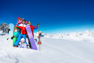 Group of young adults snowboarders pose together on top of the mountain over snow covered peaks on...