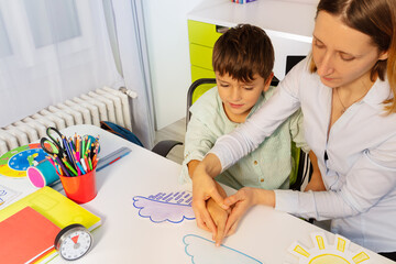 Boy with autism spectrum disorder learn weather using cards, teacher hold hands and point to correct one view from above