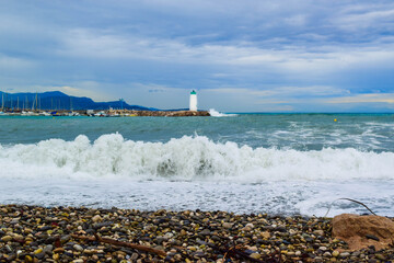 Waves crashing on on breakwater with lighthouse near the marina. Villeneuve-Loubet. France.