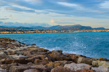 Fototapeta na wymiar Waves crashing on the rocky breakwater against the backdrop of the Mediterranean sea and the Nice city background. France.