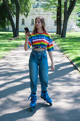 Very beautiful girl on roller skates in headphones, with a smartphone in a city park, listening to music or talking