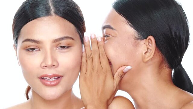 Closeup faces ot two beautiful Asian women gossiping over white background. Friend telling a secret to girlfriend whispering to ear