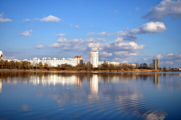 on the shore of the lake is a city that is reflected along with the sky and clouds in the water