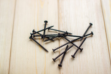 Black large screws or self-tapping screws made of high-strength steel for wooden products lie on a wooden background.