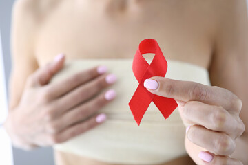 Woman's hand holds red ribbon in her hand and holds other hand on her chest in bandage. Breast...