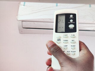 Indian man adjusting temperature of air conditioner by remote in room. Setting 21°c temperature.